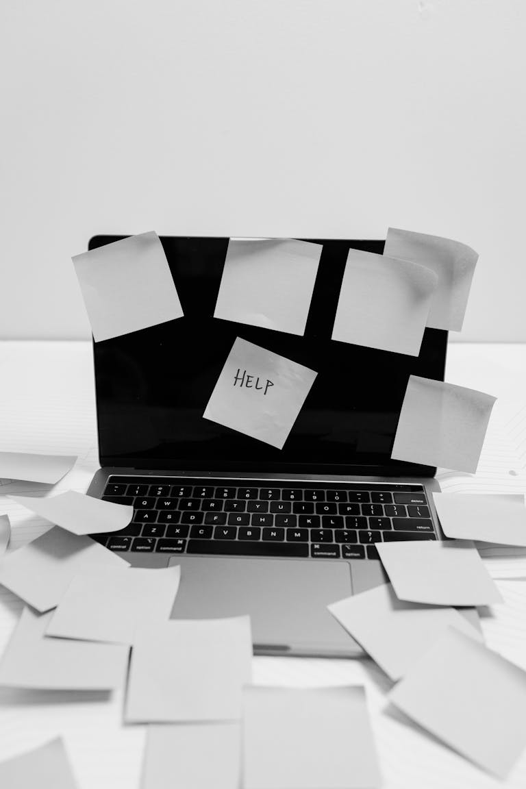 Black and white photo of a laptop covered with sticky notes, one labeled 'HELP'.