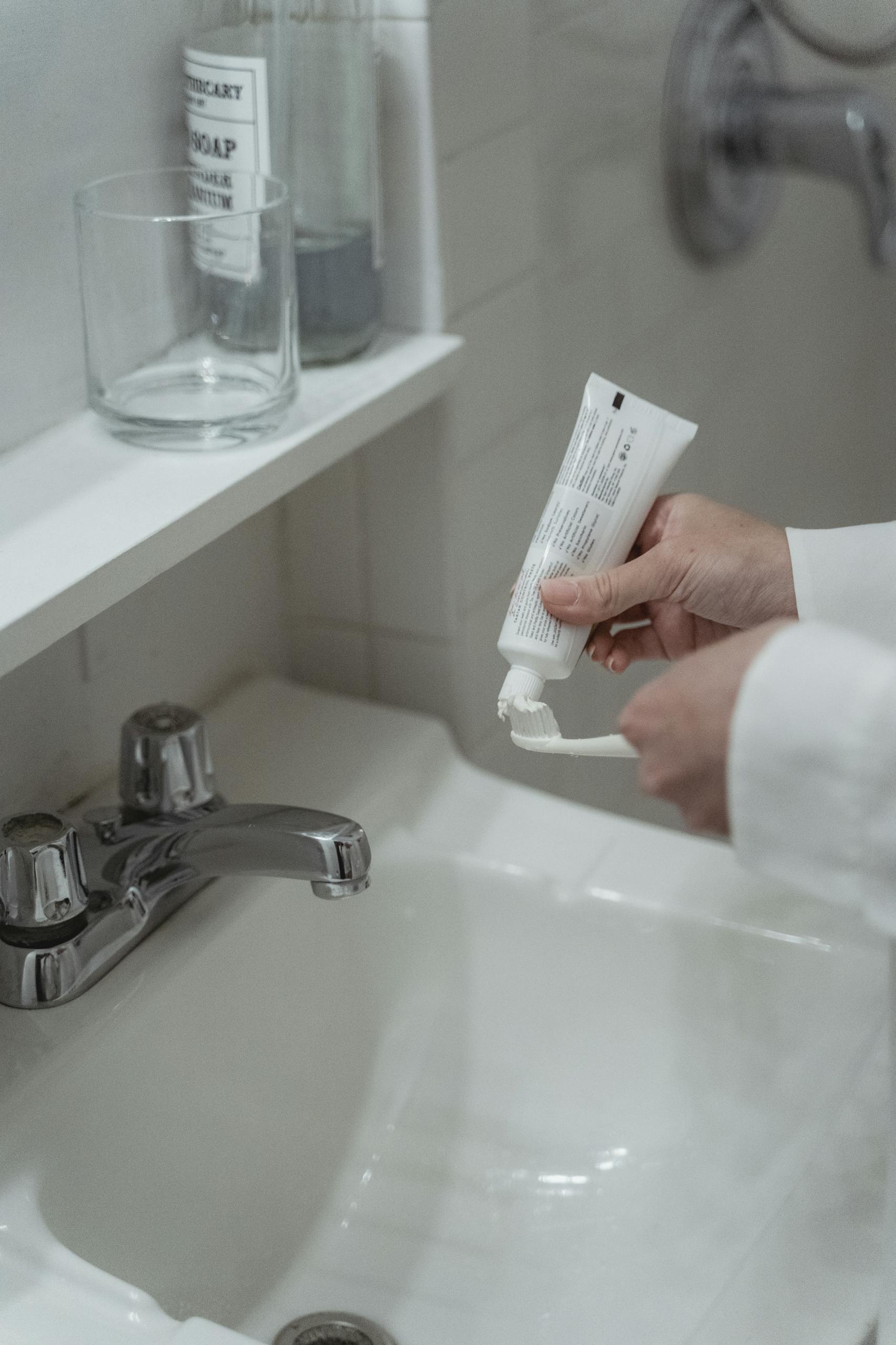 Close-up of a person applying toothpaste on a toothbrush in a clean, modern bathroom setting.