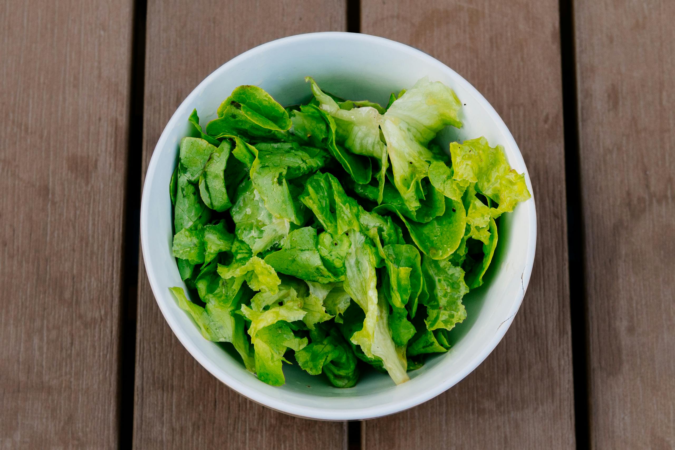 Crisp green lettuce in a white bowl on a rustic wooden surface. Perfect for healthy eating.