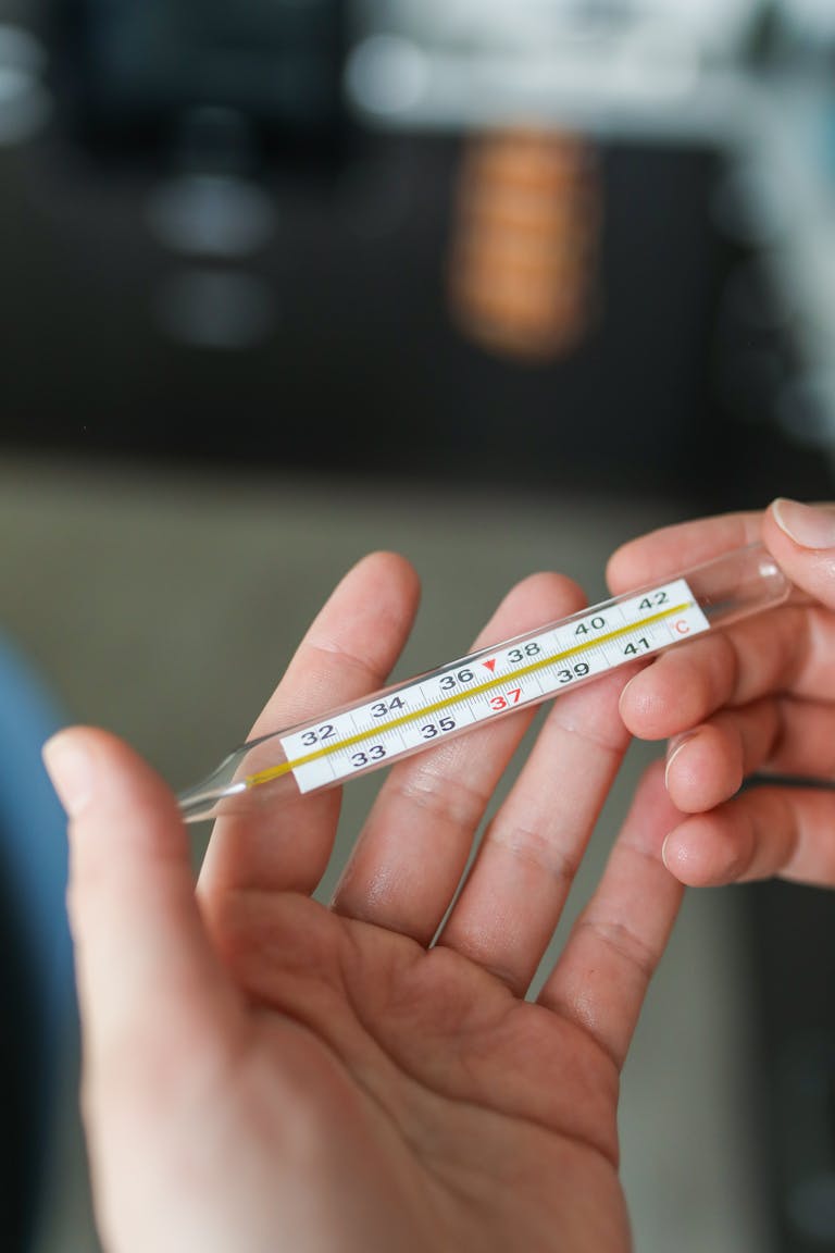 Close-up of hands holding a glass thermometer showing a high temperature.