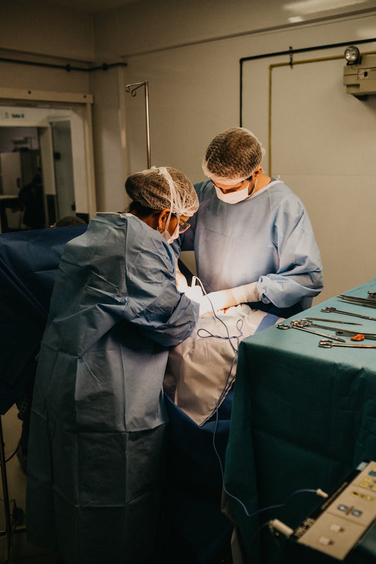 Two surgeons in an operating room conducting surgery under bright lights.