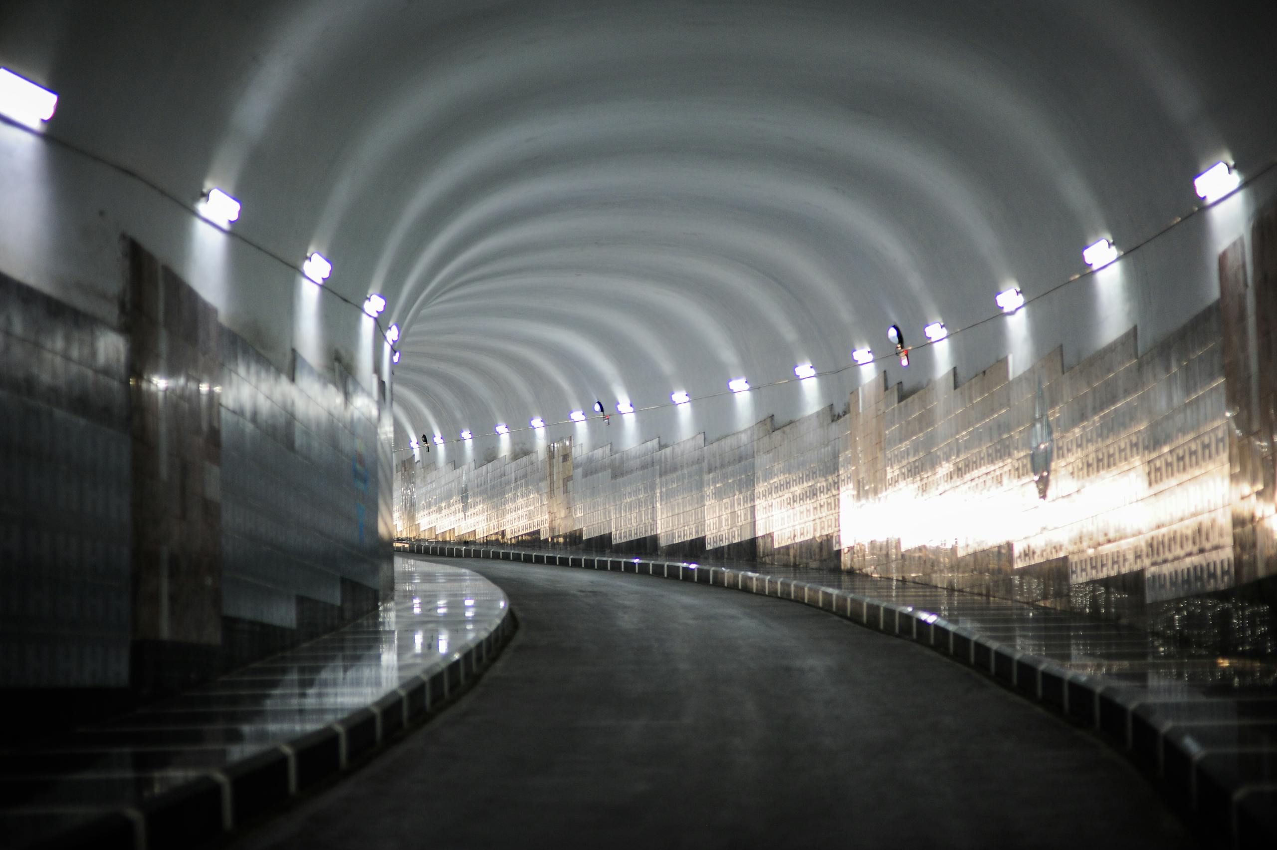 Curved road tunnel with reflective lights illuminating smooth walls in a mysterious setting.
