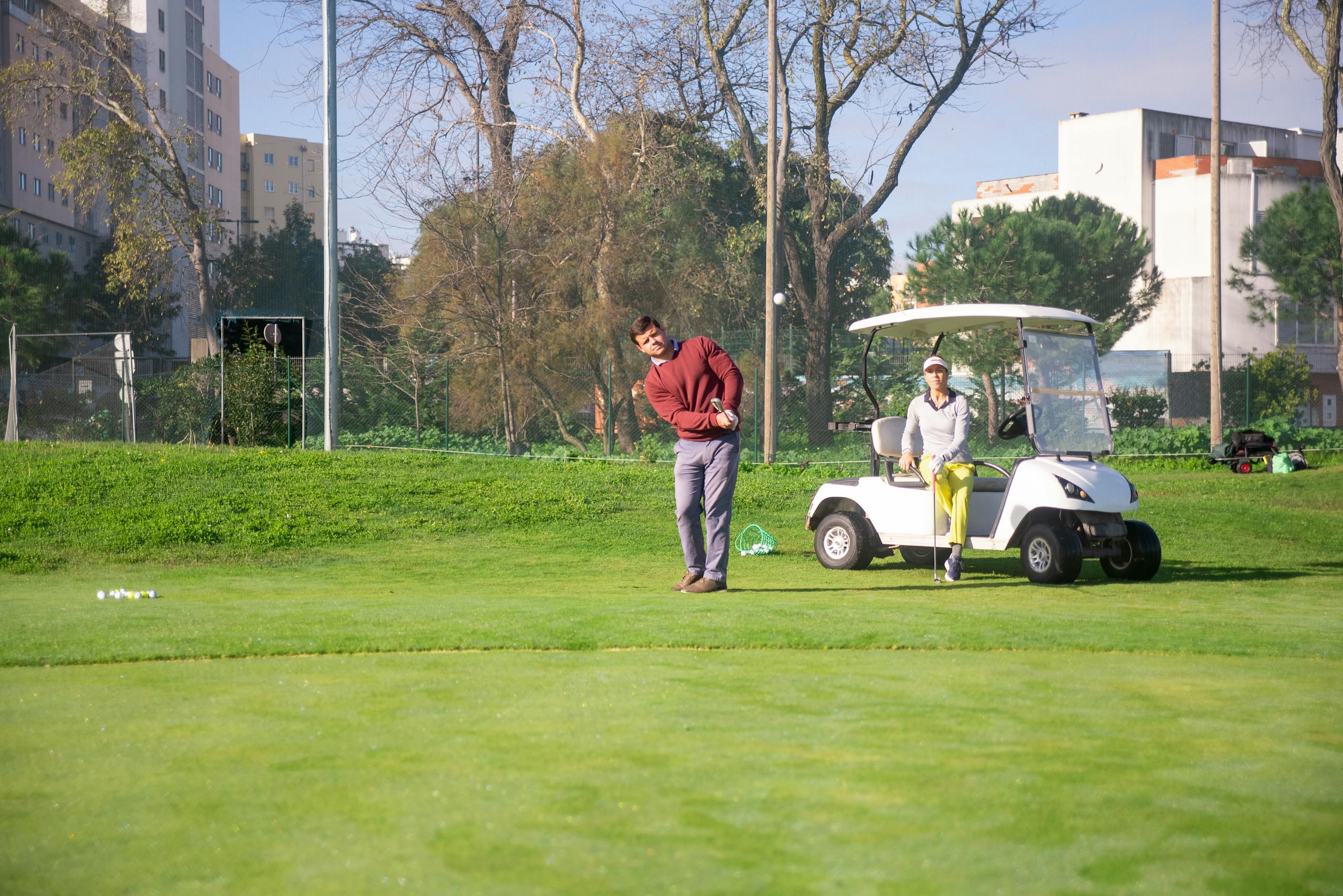Two adults playing golf on a sunny day, using a golf cart at a lush green course.