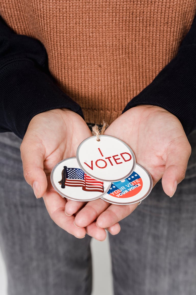 Close-up of hands holding 'I Voted' badges with USA flag, symbolizing democratic participation.