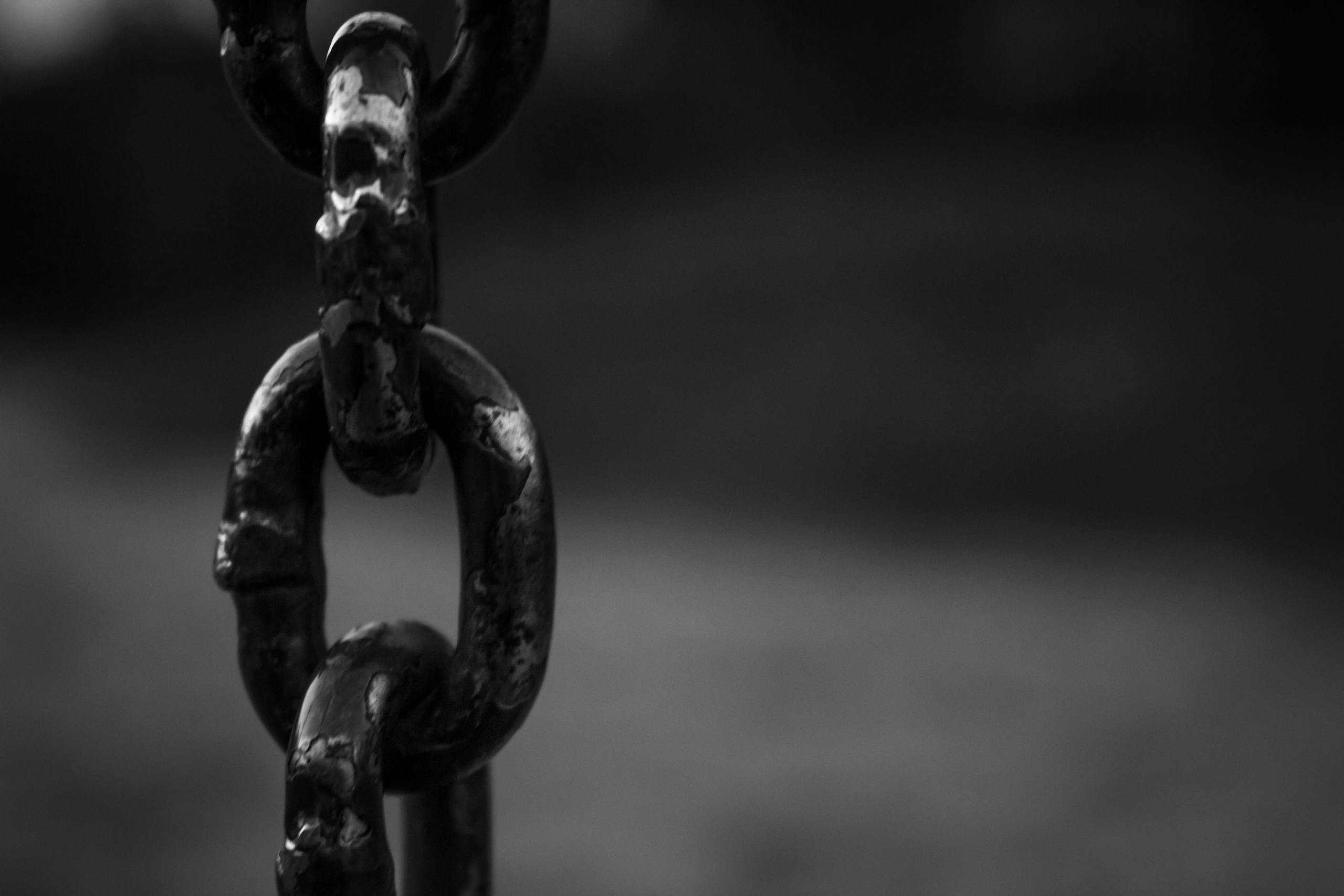 Detailed black and white image of a rusty chain link with blurred background.