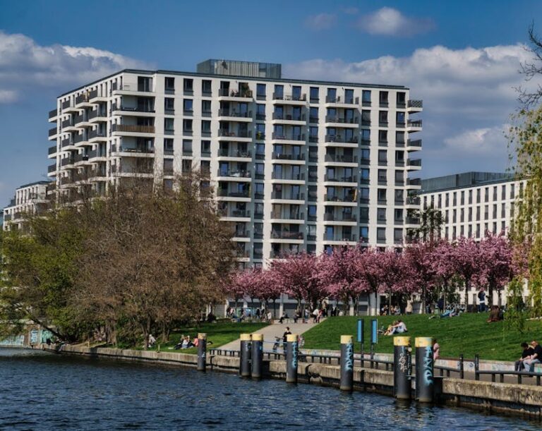 Gravel parking lot behind a Berlin apartment building with parked cars and a small green strip.