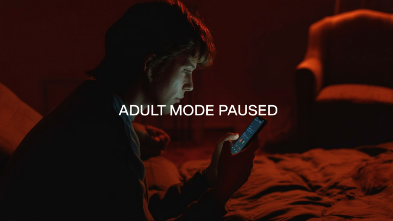 Person alone at night, dimly lit by a smartphone screen; editorial image with caption 'ADULT MODE PAUSED' at the bottom