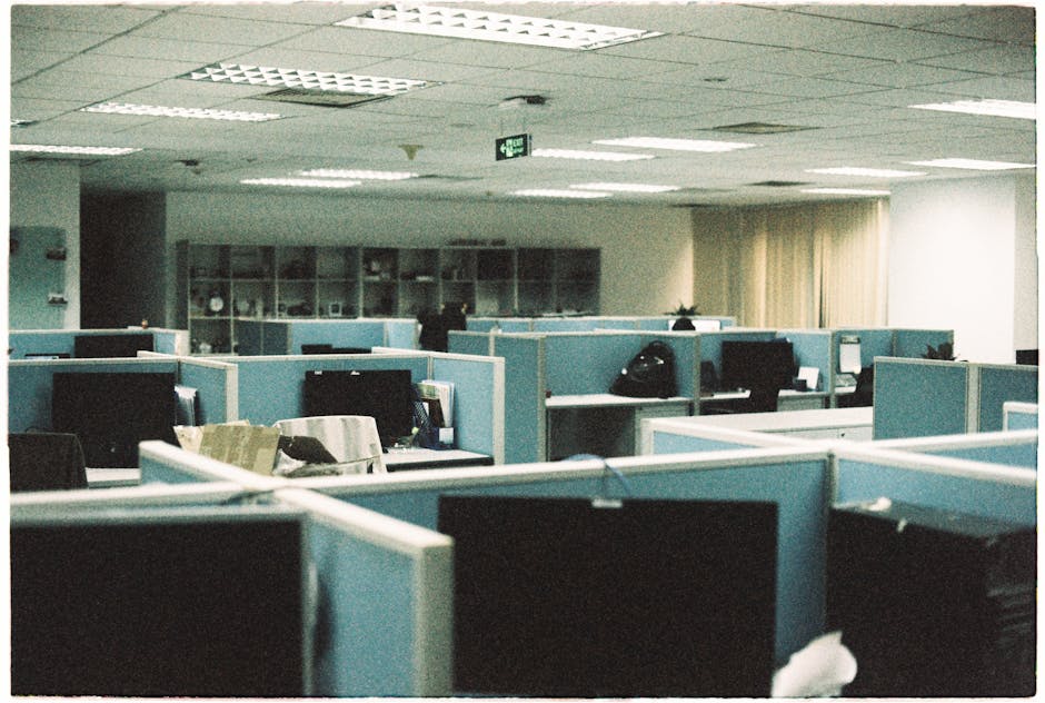 Empty modern tech office with rows of desks and computers, lights off.