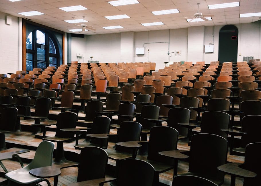 An empty university lecture hall with rows of seats and a blank projector screen, suggesting unused campus space.