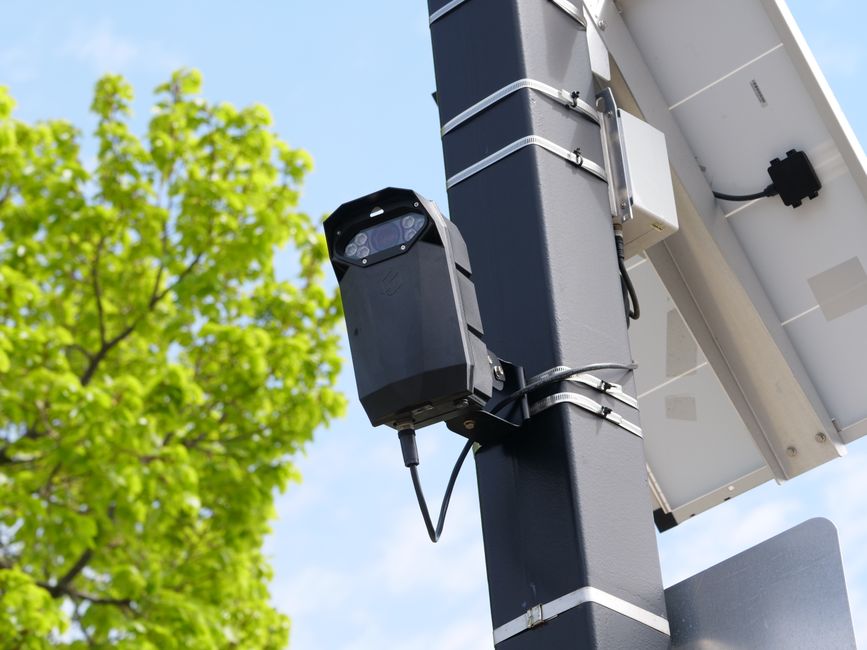 A license plate reader camera overlooking a Boston street beside a police cruiser.
